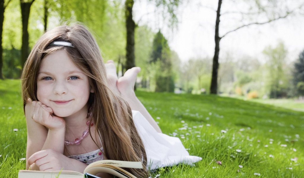 Маленькая девочка с книгой лежит на зеленой траве