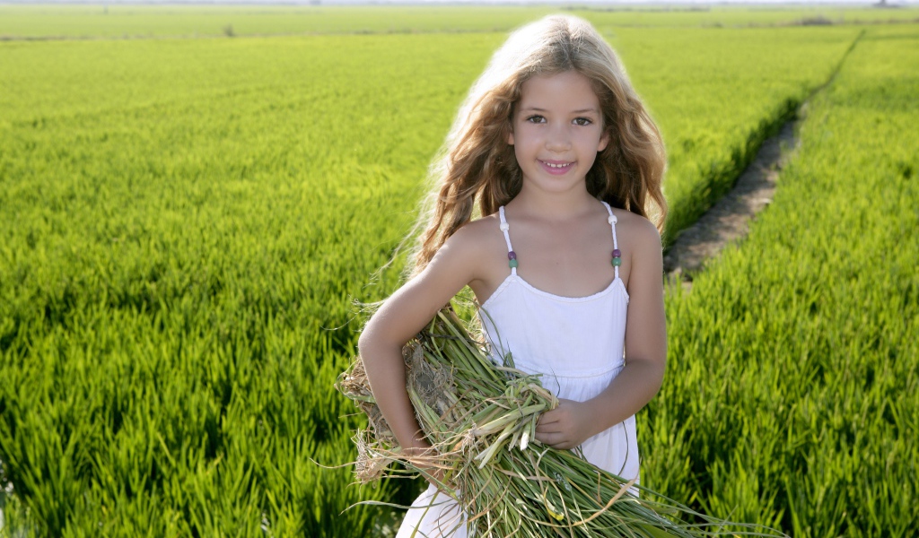 Маленькая девочка с травой в руках на поле