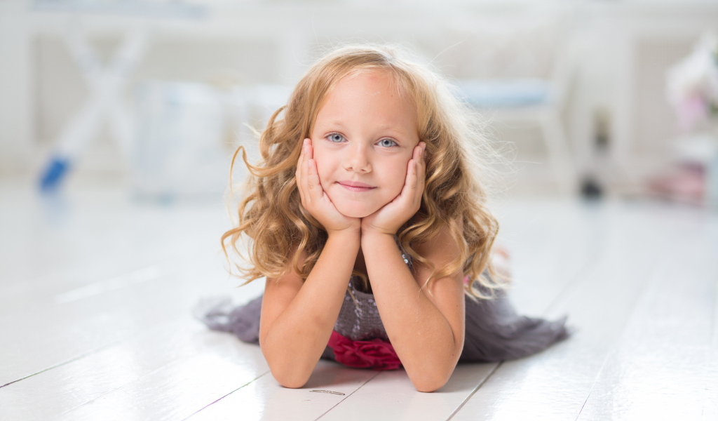 Маленькая длинноволосая голубоглазая девочка лежит на полу