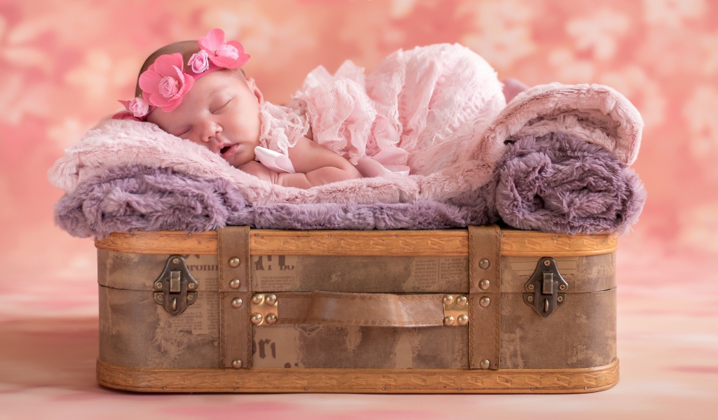 Маленькая новорожденная девочка спит на чемодане