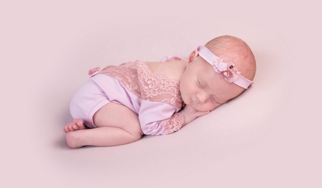Маленькая новорожденная девочка с повязкой на голове на розовом фоне