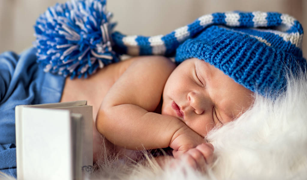 Маленький спящий грудной ребенок в синей вязанной шапке 