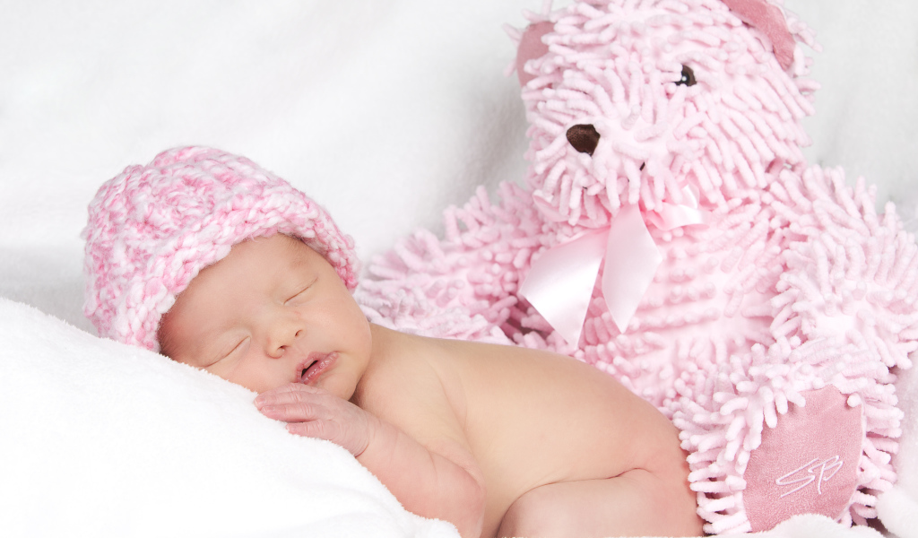 Маленький спящий ребенок в розовой шапке с игрушечным мишкой