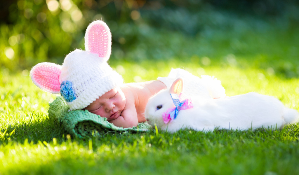Маленький спящий грудной ребенок на зеленой траве с белым кроликом