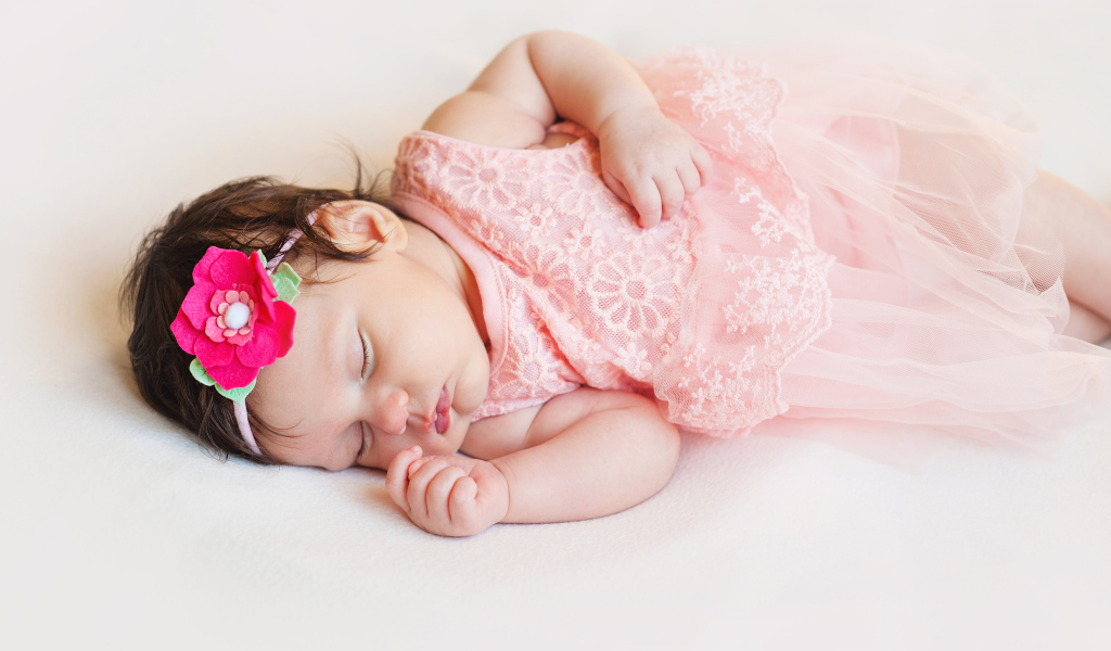 Маленькая спящая девочка в розовом платье с цветком в волосах 
