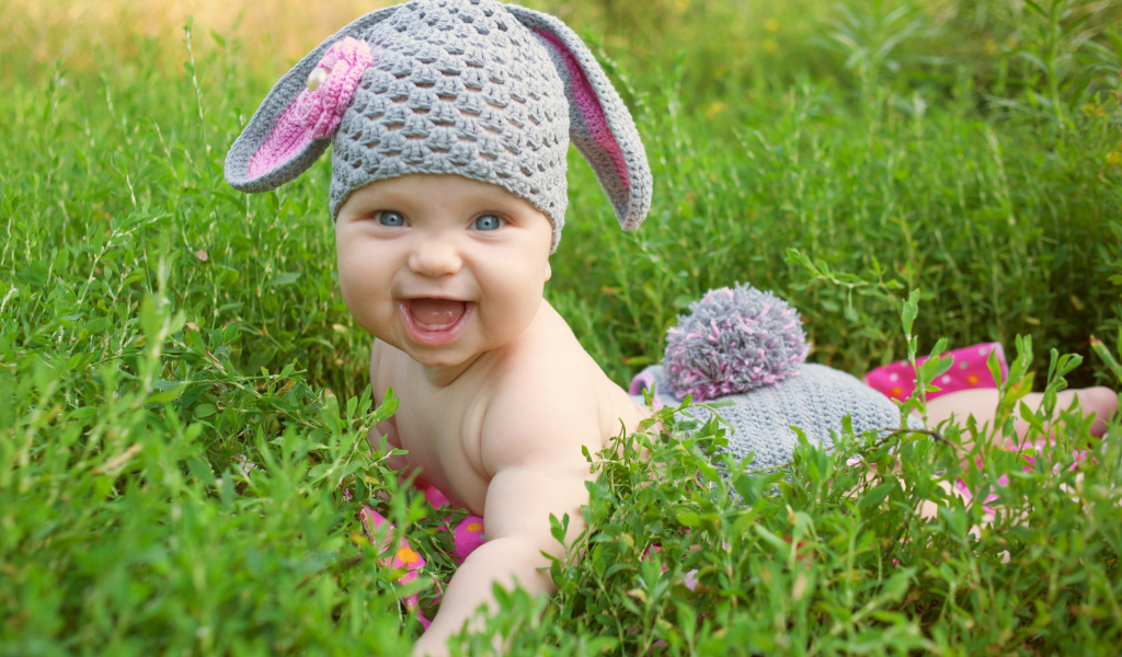 Маленький улыбающийся ребенок в костюме зайчика лежит в зеленой траве