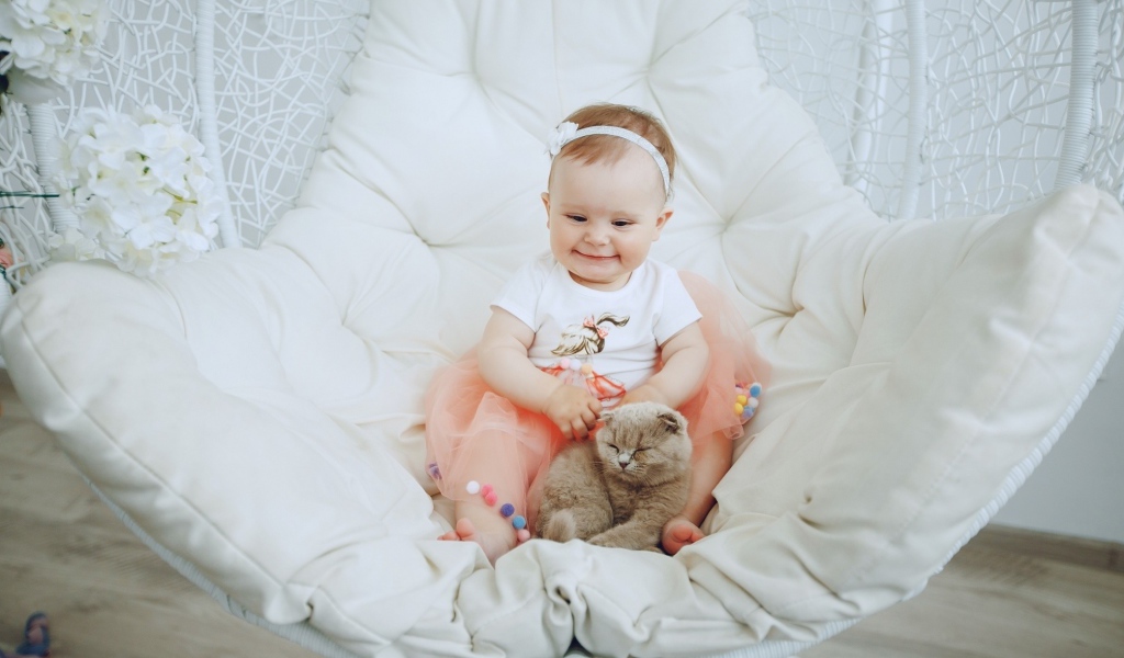 Маленький улыбающийся ребенок с котом сидит в белом кресле