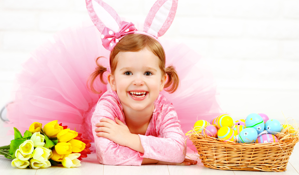 Маленькая улыбающаяся девочка в розовом с пасхальными яйцами и букетом тюльпанов