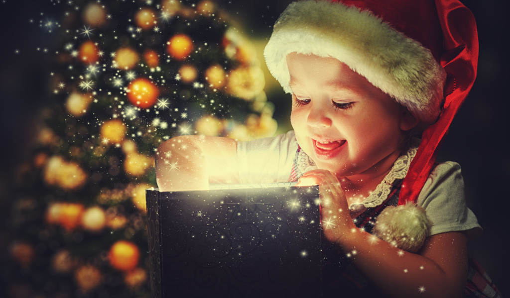 Маленькая улыбающаяся девочка открывает подарок у новогодней елки 