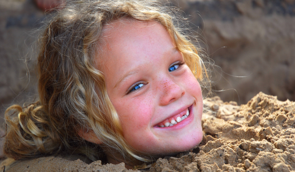 Маленькая улыбающаяся девочка играет в песке