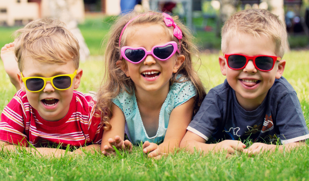 Улыбающиеся мальчики и девочка лежат на зеленой траве