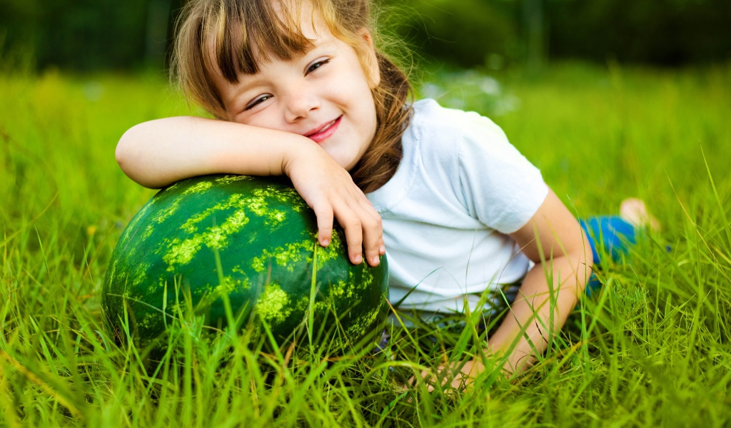 Улыбающаяся девочка с зеленым арбузом на траве