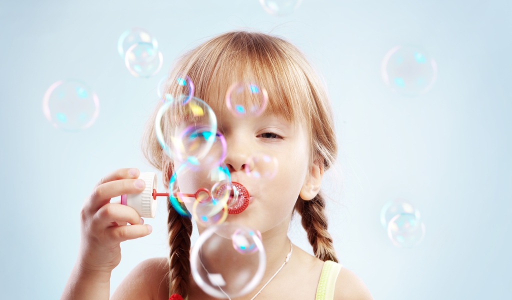 Девочка с косичками пускает мыльные пузыри