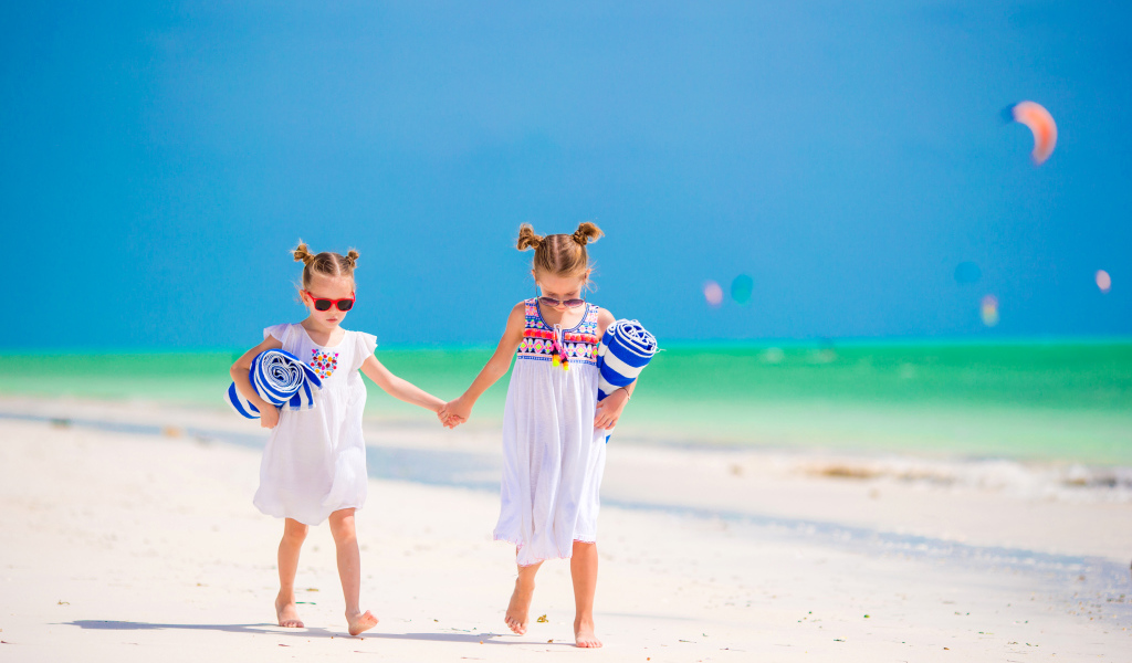 Две маленькие девочки идут по песку