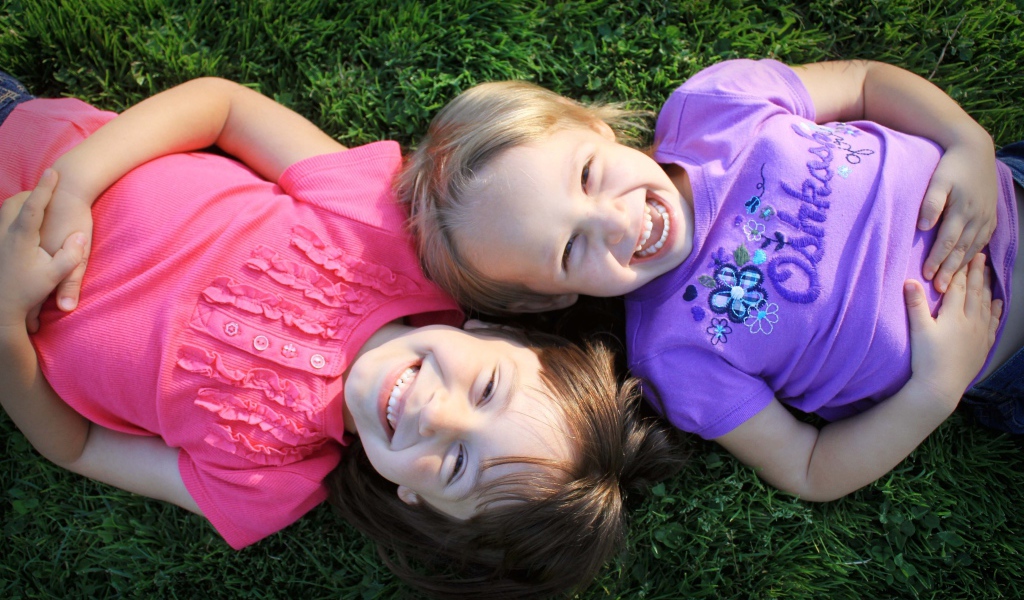 Две маленьких улыбающихся девочки лежат на зеленой траве