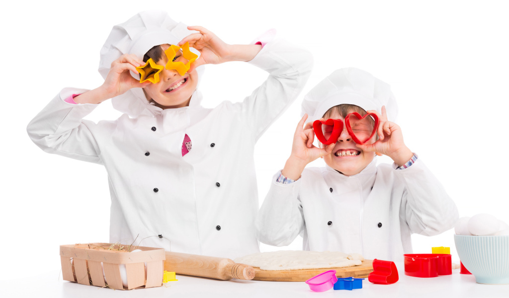 Два маленьких ребенка в костюмах повара готовят на кухне печенье