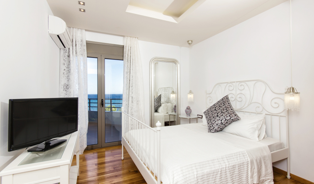 Светлая спальня с большой белой кроватью и телевизором 