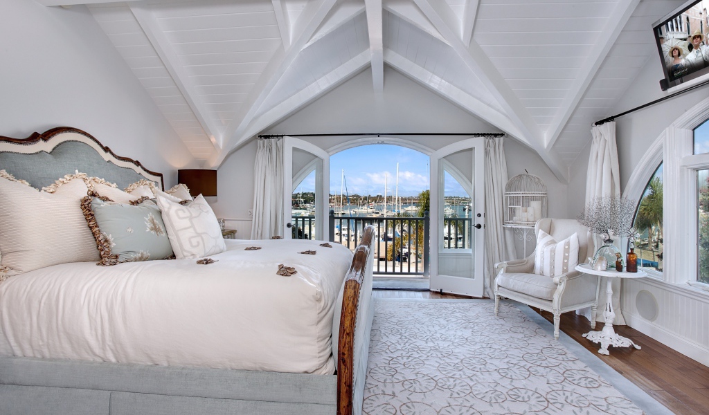 Белая спальня с большой высокой кроватью и балконом 