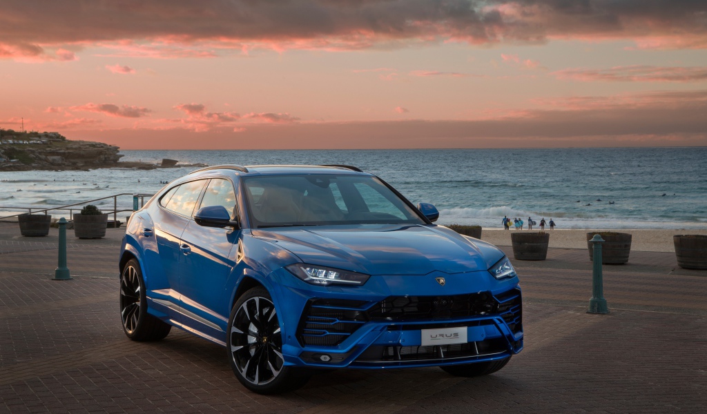 Синий автомобиль Lamborghini Urus под пасмурным небом на берегу  океана
