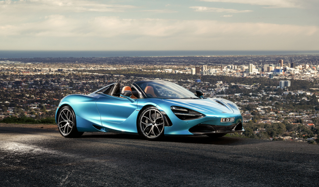 Голубой спортивный автомобиль McLaren 720S Spider 2019 года на фоне города