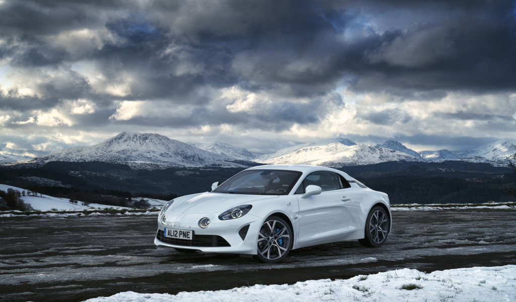Белый автомобиль Alpine A110 на фоне гор под грозовым небом  