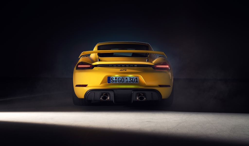 Желтый автомобиль Porsche 718 Cayman GT4, 2019 года вид сзади на сером фоне
