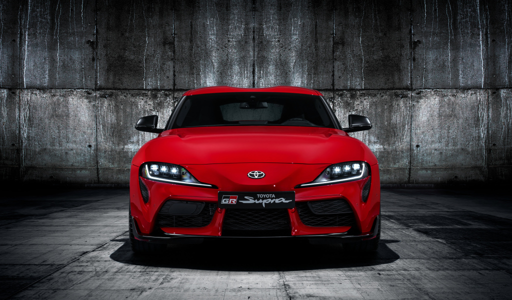 Красный автомобиль Toyota GR Supra 2019 года на фоне серой стены