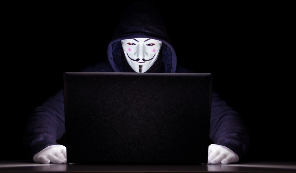 Хакер анонимус в маске и худи за ноутбуком