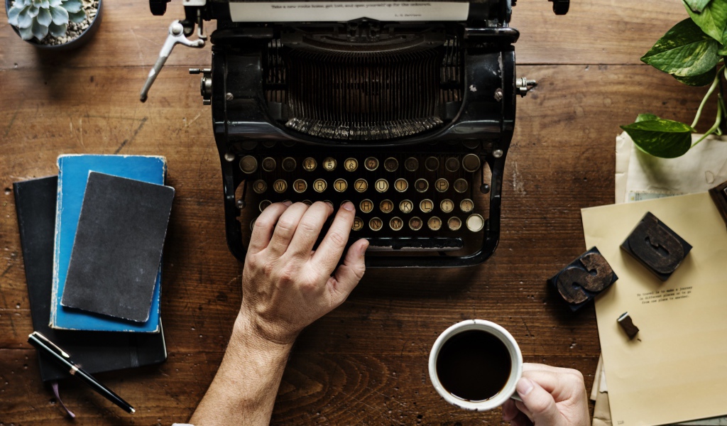 Мужчина с чашкой кофе в руке печатает на старой печатной машинке 