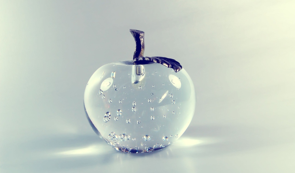 Стеклянное яблоко на сером фоне 