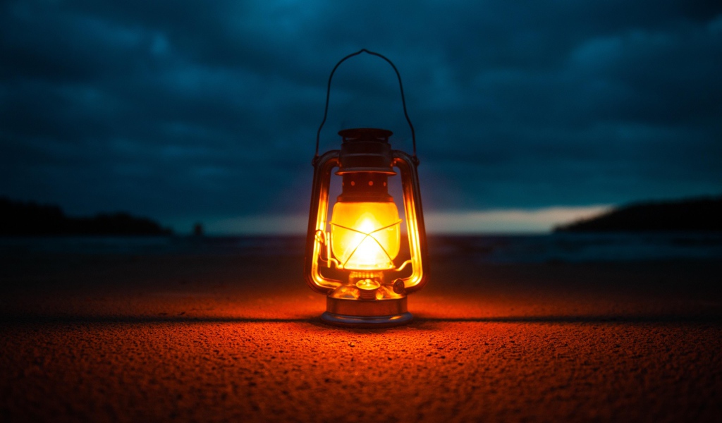 Включенный фонарь стоит на песке у моря 