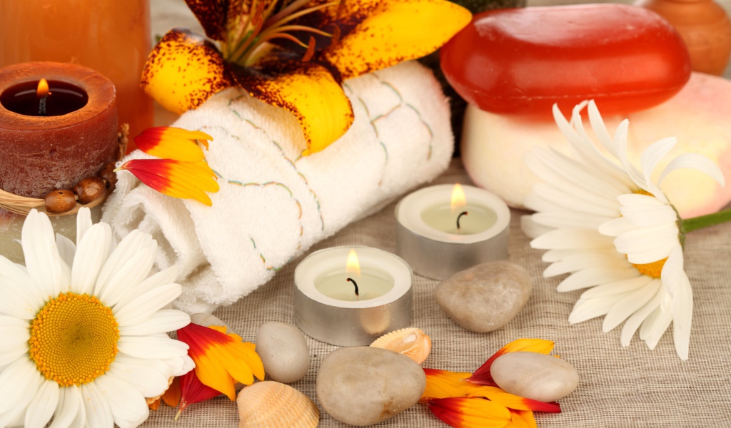 Зажженные свечи на столе с полотенцем, цветами и мылом