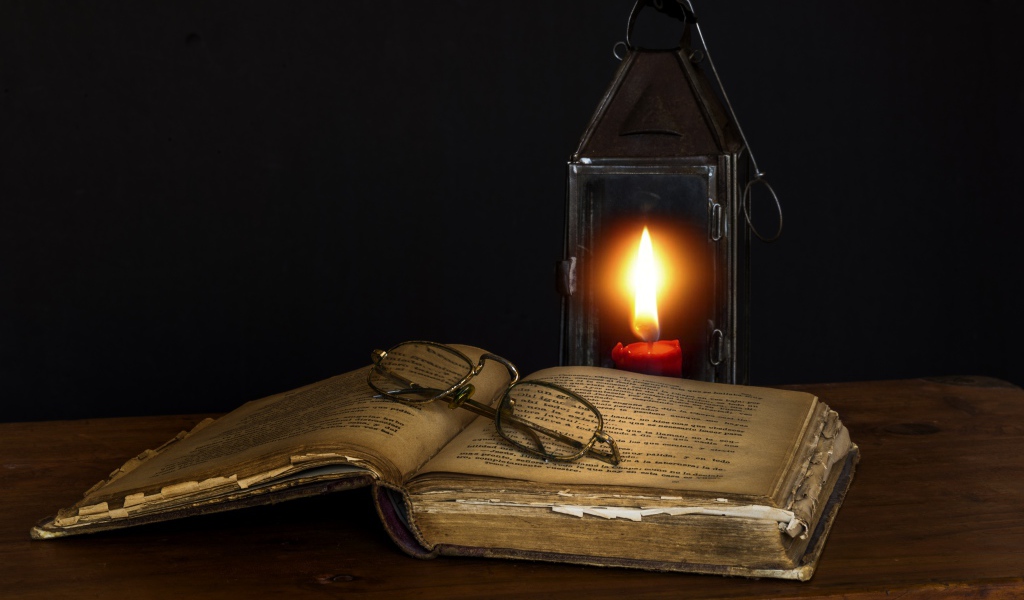Старая книга с очками на столе со свечой 