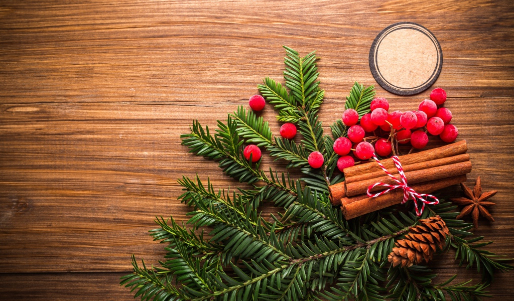 Еловая ветка, корица, ягоды рябины и шишки на деревянном фоне