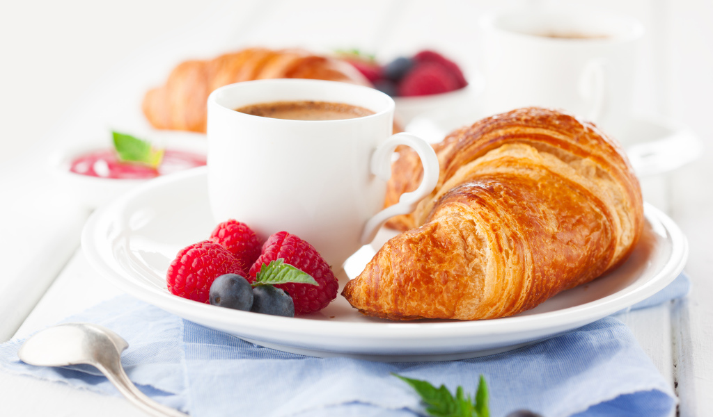 Чашка кофе на тарелке с круассаном и ягодами