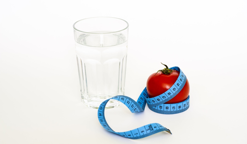 Стакан воды на белом фоне с красным помидором и сантиметром