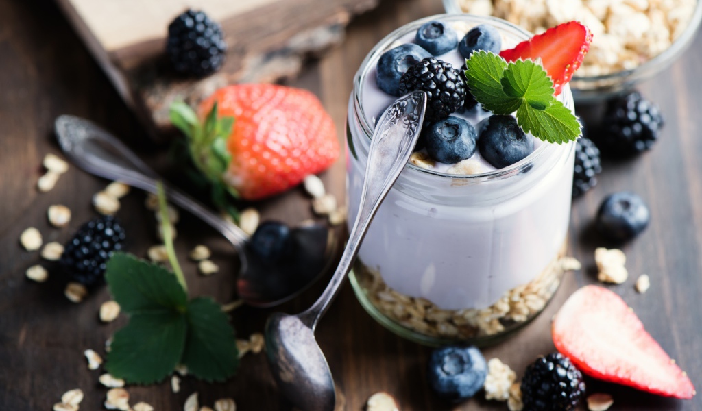 A jar of cereal, yogurt and berries on the table with spoons