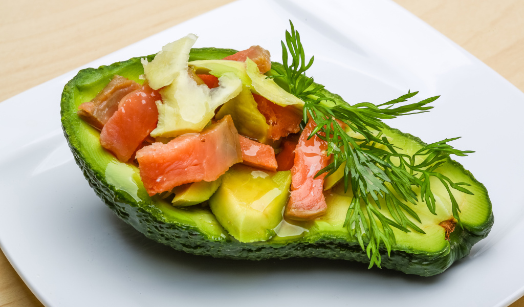 Авокадо с салатом из красной рыбы на белой тарелке