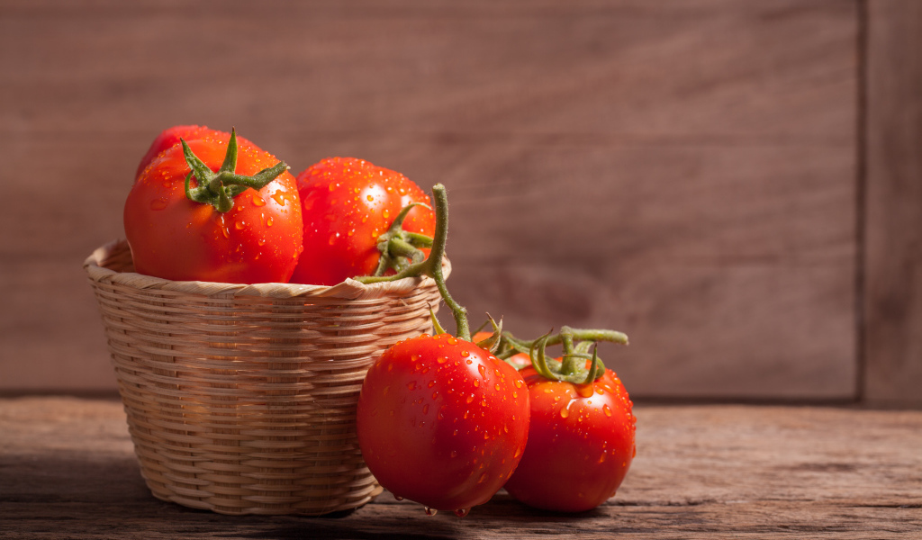 Красивые красные мокрые помидоры в корзине на столе 