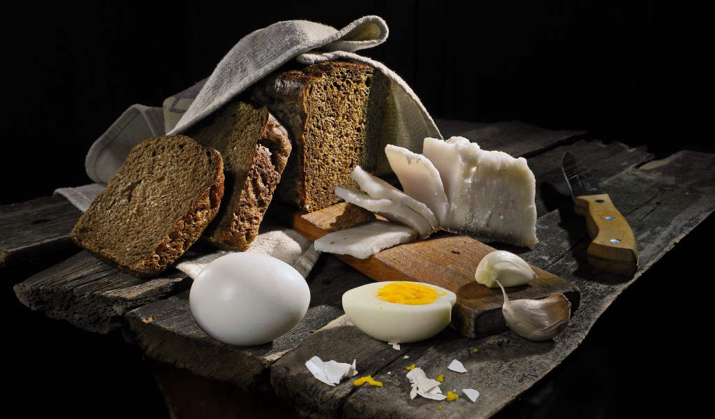 Черный хлеб, вареные яйца, чеснок и сало на деревянном столе