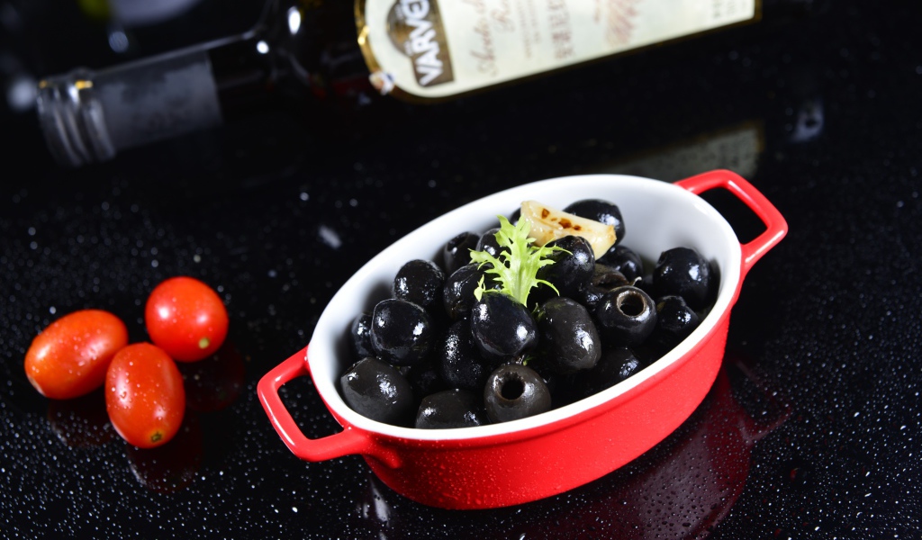 Черные оливки на столе с бутылкой и помидорами