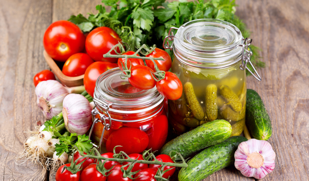 Консервированные помидоры и огурцы на столе со свежими овощами и зеленью 