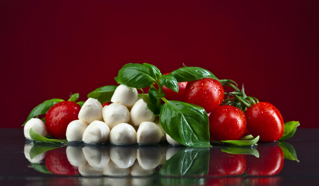 Сыр на столе с зеленью базилика и красными помидорами