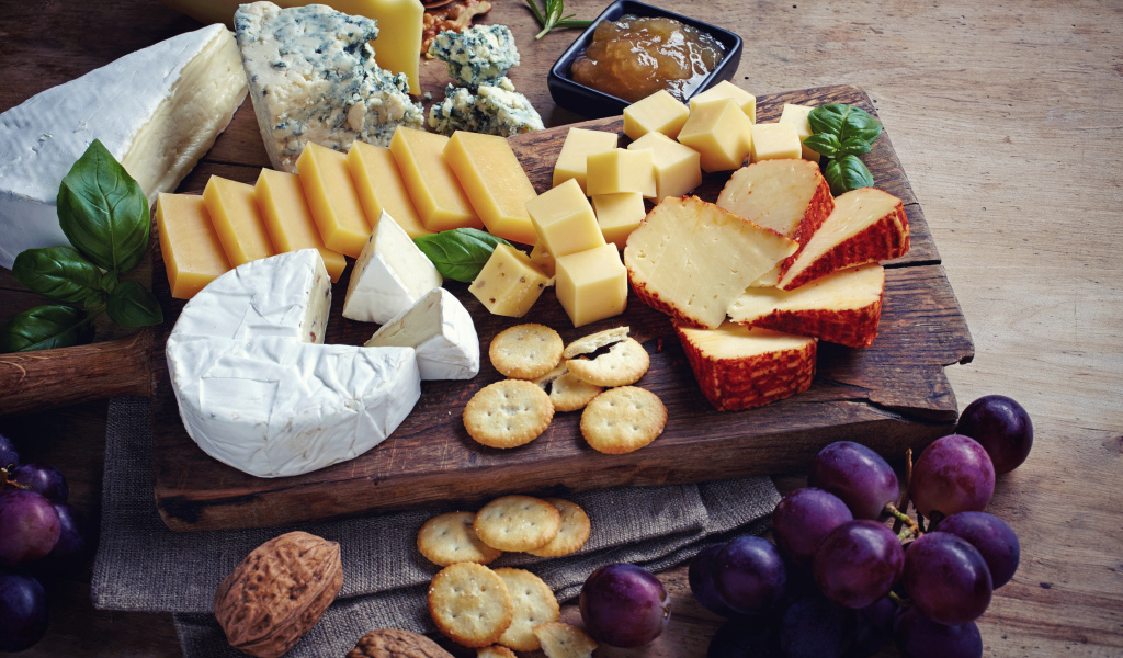 Сырная нарезка на разделочной доске на столе с виноградом и крекерами
