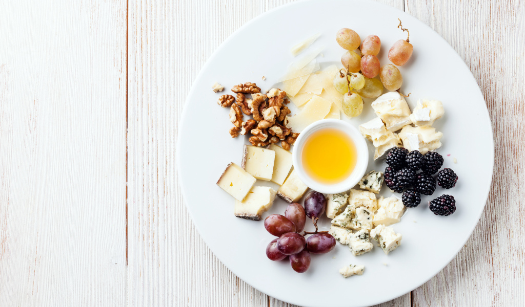 Куски сыра на тарелке с орехами, виноградом, медом и ягодами ежевики