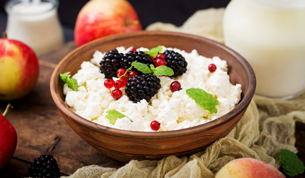 Творог с ягодами в деревянной миске на столе с яблоками