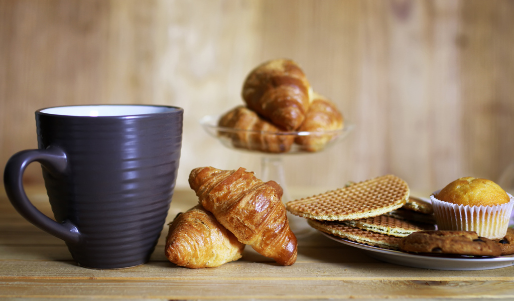 Чашка на столе с круассанами и вафлями 