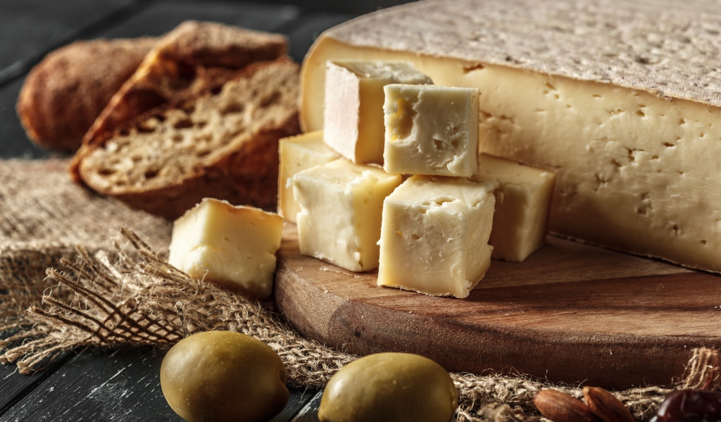 Сыр нарезан кубиками на столе с хлебом и оливками