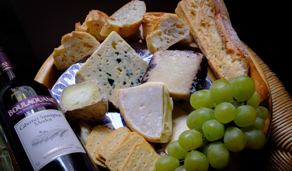 Разные виды твердого сыра на тарелке с белыми виноградом и вином