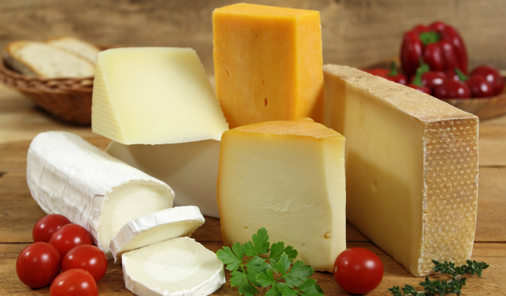 Разные виды твердого сыра на столе с помидорами и петрушкой